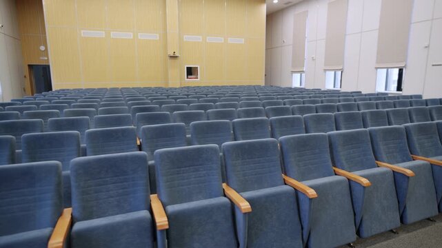 Auditorium stands empty with multiple lines of soft conference seats. Assembly hall design provides spacious environment for students