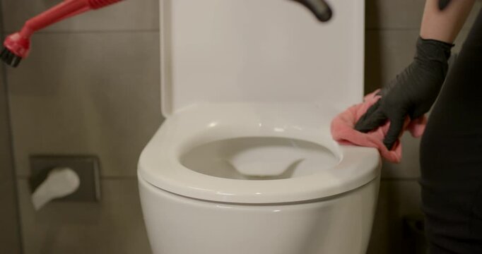 Worker in black gloves wiping chrome washbasin faucet with yellow cloth during bathroom sanitization