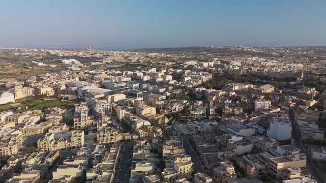 In Victoria on Gozo island, a drone view captures the historic city's dense Maltese architecture, streets lined with storefronts, pedestrians, and vehicles.