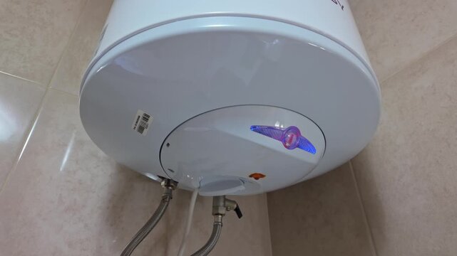 In a residential utility room, a rusty electric water heater shows active leakage from its tank and fittings, with moisture and stains visible around the plumbing in a close-up view.