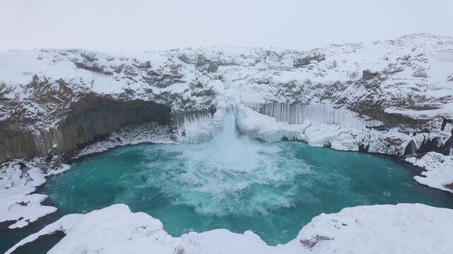 View of the frozen Aldeyjarfoss waterfall with turquoise water flowing between snow-covered basalt columns in the Icelandic highlands, Iceland.
