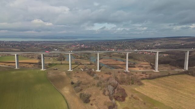In Somogy County, Hungary, the Kőr&ouml;shegyi V&ouml;lgyh&iacute;d viaduct carries M7 highway traffic across a rural landscape near Lake Balaton in an aerial wide shot under a cloudy winter sky.