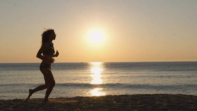 A young woman runs on the beach during sunrise, embracing an active and healthy lifestyle. The tranquil ocean and soft sunlight create a serene and inspiring scene
