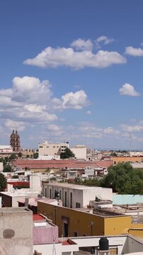 View of the historic Cathedral of Durango rising above the city rooftops under a bright blue sky with scattered clouds in Durango, Durango, Mexico.