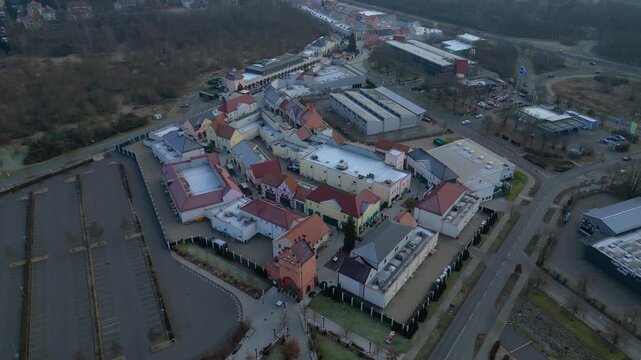 A large shopping outlet center with multiple buildings, retail stores, and an empty parking lot. Smooth aerial view drone top down Above view