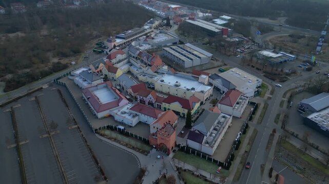 A large shopping outlet center with multiple buildings, retail stores, and an empty parking lot. Fantastic aerial view panorama orbit overview drone