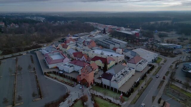 A large shopping outlet center with multiple buildings, retail stores, and an empty parking lot. Dramatic aerial view ascending raise up panorama drone