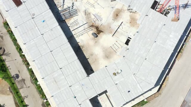 Large gray industrial building under construction dominates expansive outdoor parking lot, representing ongoing infrastructure development and commercial projects during daylight.