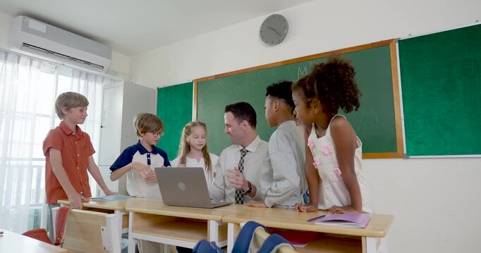 Slow motion classroom scene follows young multicultural pupil group and male adult teacher around laptop, sharing answer time, friendly highfive, teamwork and back to school learning routine