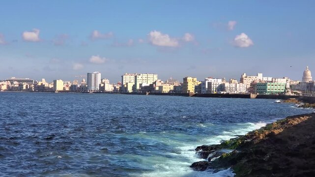 View of the Malecon coastline with historic buildings and the Capitolio dome in the background under a clear blue sky in Havana, Havana, Cuba.