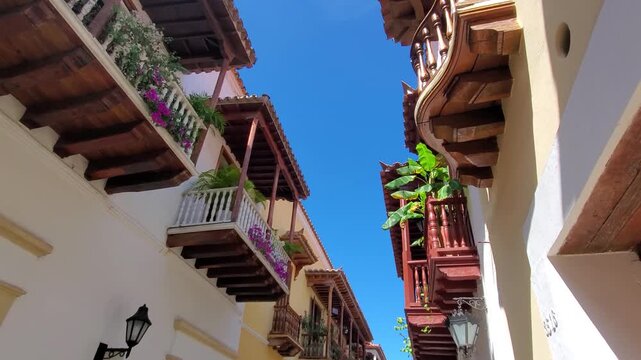 View of colorful colonial balconies adorned with flowers in the historic Getsemani neighborhood under a clear blue sky in Cartagena, Bolivar, Colombia.