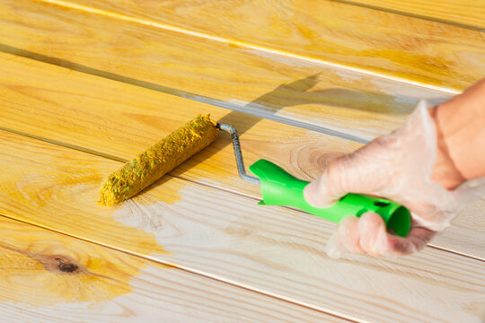 Wood preservative treatment applied with paint roller on natural timber boards. Wood protection, surface coating, waterproofing and anti-rot maintenance concept for construction and renovation.