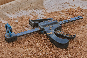 Obraz premium Plastic woodworking clamp rests on wooden workbench covered in sawdust. Carpentry work. Concept diy tutorials, furniture making, joinery services, tool and home renovation.