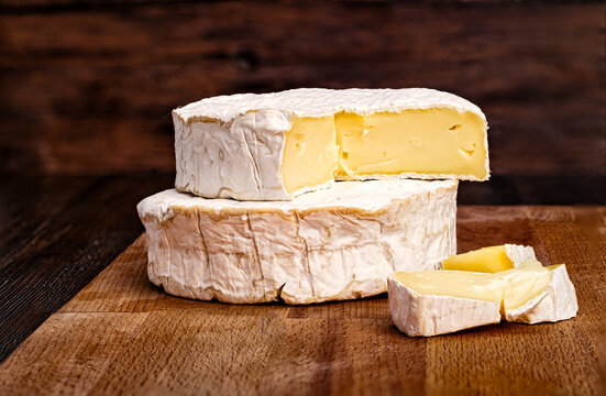 Whole and sliced Camembert cheese on rustic wooden board with dark background