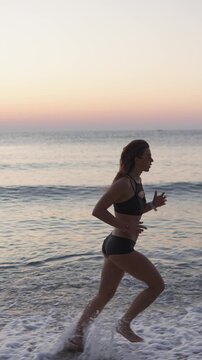 Confident female runner exercises on the beach during a beautiful sunrise, creating an inspiring fitness scene. Healthy lifestyle and outdoor activity concept with ocean and pastel sky background