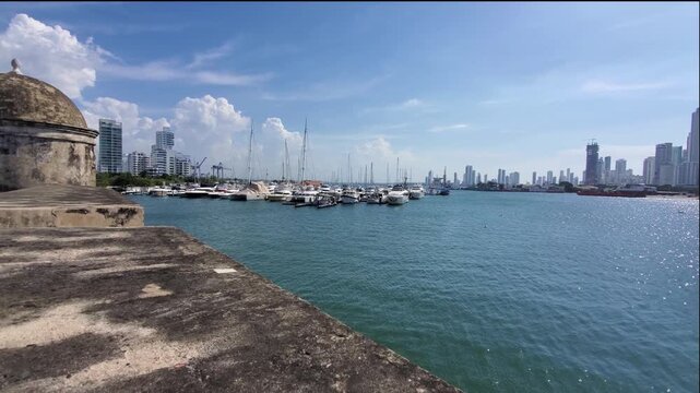 View of the historic stone watchtower overlooking the marina with yachts and the modern skyline of Bocagrande in Cartagena, Bolivar, Colombia.