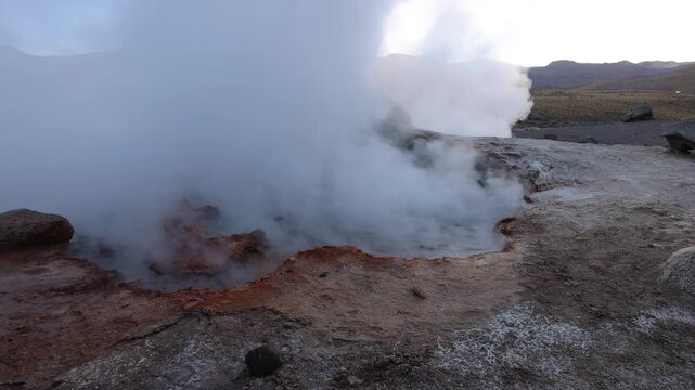 View of steam rising from the El Tatio geyser field with volcanic soil and rocky terrain in San Pedro de Atacama, Antofagasta, Chile.