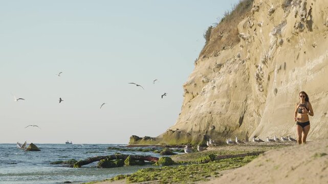 Athletic female runner enjoys a morning workout by the sea, surrounded by nature and fresh air. The dramatic cliffs and ocean waves highlight a healthy, active outdoor lifestyle