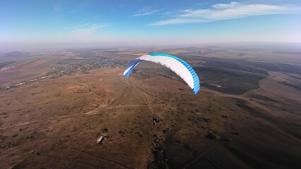 Paraglider flying over open landscape with blue sky © TamasSzora
