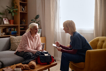 Side view of senior Caucasian woman consulting home healthcare nurse, discussing care plan and treatment notes in living room. Useful for elder care, home visit, patient support marketing © Seventyfour