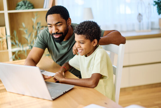 Father and son doing homework with laptop at home. Father and teenage son using laptop. Boy and dad sitting at home working with notebook