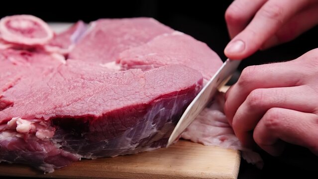 Person slicing raw beef steak with knife on cutting board