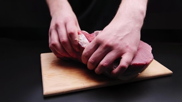 Person slicing raw beef steak on wooden cutting board