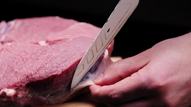 Person slicing raw meat with a knife on a dark surface