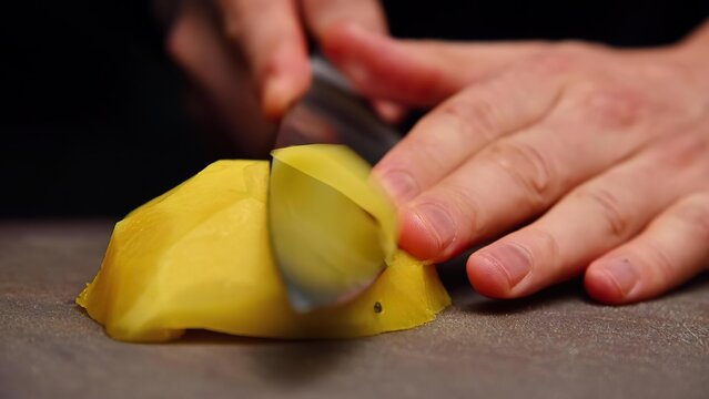 Person slicing yellow squash on a gray cutting board