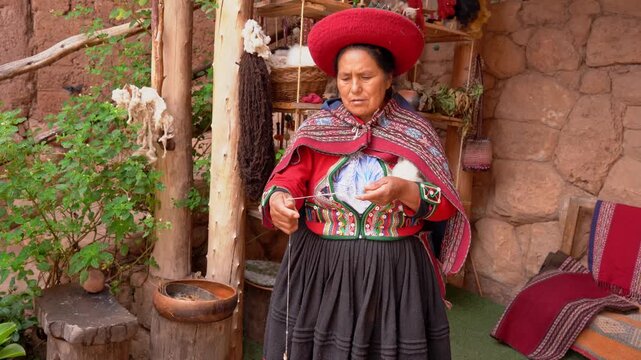 Peruvian senior woman spinning alpaca wool with a traditional spindle