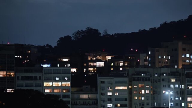 View of illuminated residential buildings in the Flamengo neighborhood at night, with warm lights glowing in windows against a dark hillside in Rio de Janeiro, Rio de Janeiro, Brazil.