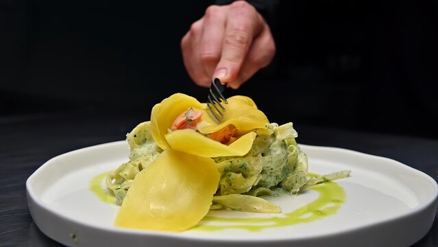 Person's hand with fork eating vegetable pasta dish