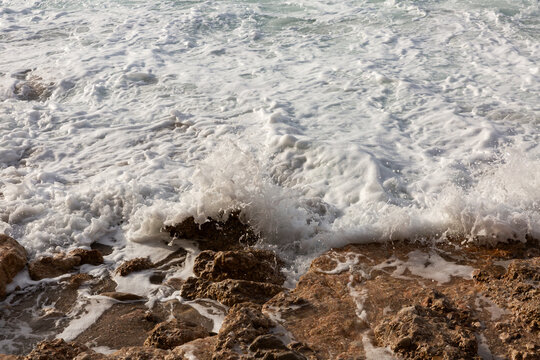 Bord de mer, gros plan sur une vague qui s&rsquo;&eacute;choue et qui claque sur la roche brune en bord de plage, vue de face, &eacute;cume de mer, mousse blanche