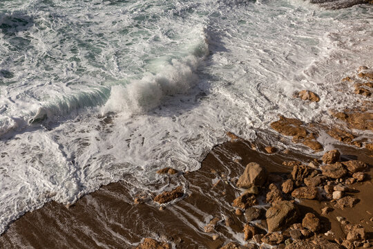 Bord de mer, gros plan sur une vague qui s&rsquo;&eacute;choue sur le sable et la roche brune, mer agit&eacute;e et vivante, &eacute;cume de mer blanche