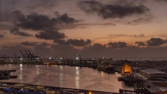 View of the Karachi Port Trust harbor at sunset with cargo cranes and ships docked along the waterfront in Karachi, Sindh, Pakistan.