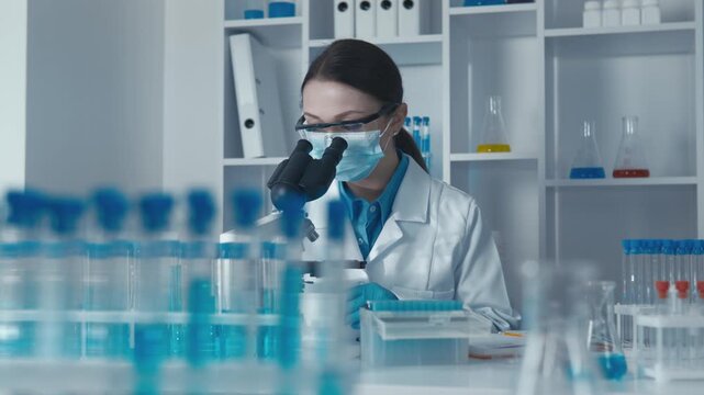 A woman researcher conducts scientific analysis using a microscope, surrounded by laboratory glassware and test tubes. The image highlights innovation, safety, and cutting edge laboratory technology