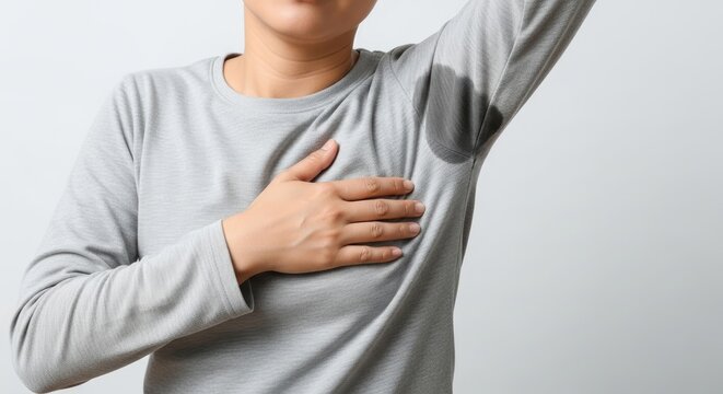 Woman in grey shirt showing underarm sweat stains, indicating hyperhidrosis, body odor, or discomfort. Close-up on a common hygiene problem.