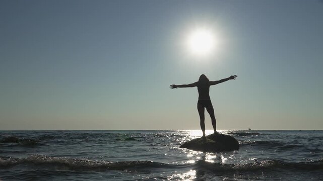 A person celebrates life on a rock surrounded by ocean waves, basking in the sunlight. The uplifting scene captures the essence of adventure, freedom, and connection with nature