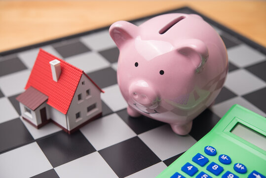 Ping piggy bank, small house and calculator on chessboard background. Financial management, planning and strategy for house buying, expense, cost of living, investment, tax payment and so on concept.