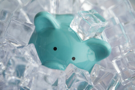 Blue piggy bank frozen in a lot of ice cube. Frozen bank account cannot withdraw, transfer or spend money due to fraud, scams, outstanding debts, etc., confiscated illegal assets and so on concept.