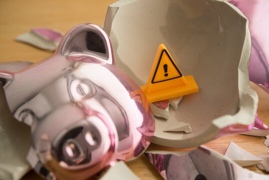 Broken piggy bank with yellow warning sign inside. No savings, poor due to many expenses, high cost of living, inflation, global economy crisis, unemployed, loss investment and so on concept.