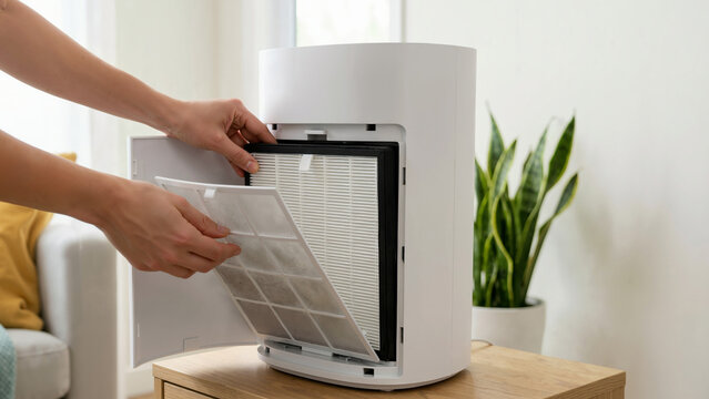 Hands replacing the HEPA filter in a modern white room air purifier. Person changing dirty filter for indoor air quality maintenance. Home appliance care concept