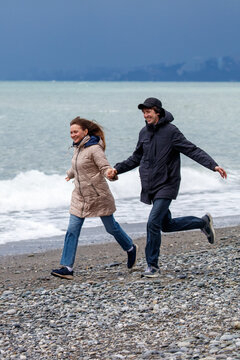 Couple runs hand-in-hand on rocky beach