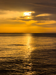Fototapeta premium Sunset over ocean water with golden reflections and soft clouds