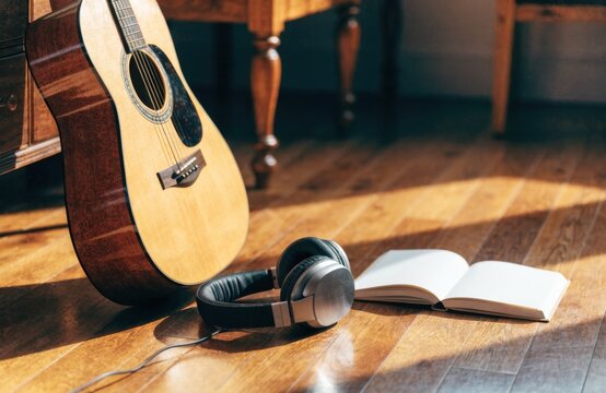 Acoustic guitar, headphones, and open book resting on a wooden floor