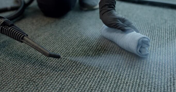 Worker placing a rolled blue microfiber cloth on carpet next to hot steam nozzle tool spraying vapor