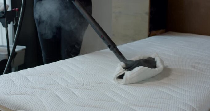 High angle view of professional steam tool with white cloth pad moving across a modern bedroom mattress
