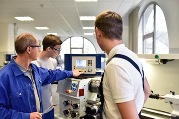 young apprentices in technical vocational training are taught by older trainers on a cnc lathes machine © industrieblick