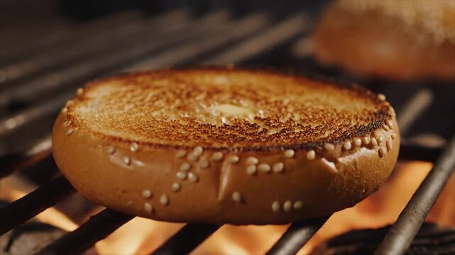 A toasted sesame seed bagel is grilled on a barbecue grate with another bagel behind.