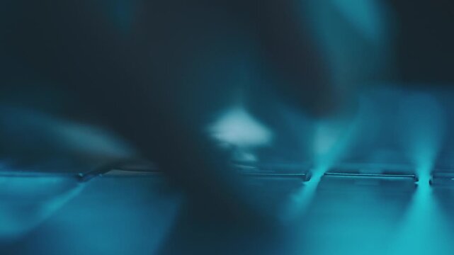 Macro view of hands typing fast on laptop keyboard with blue backlight in dark environment.